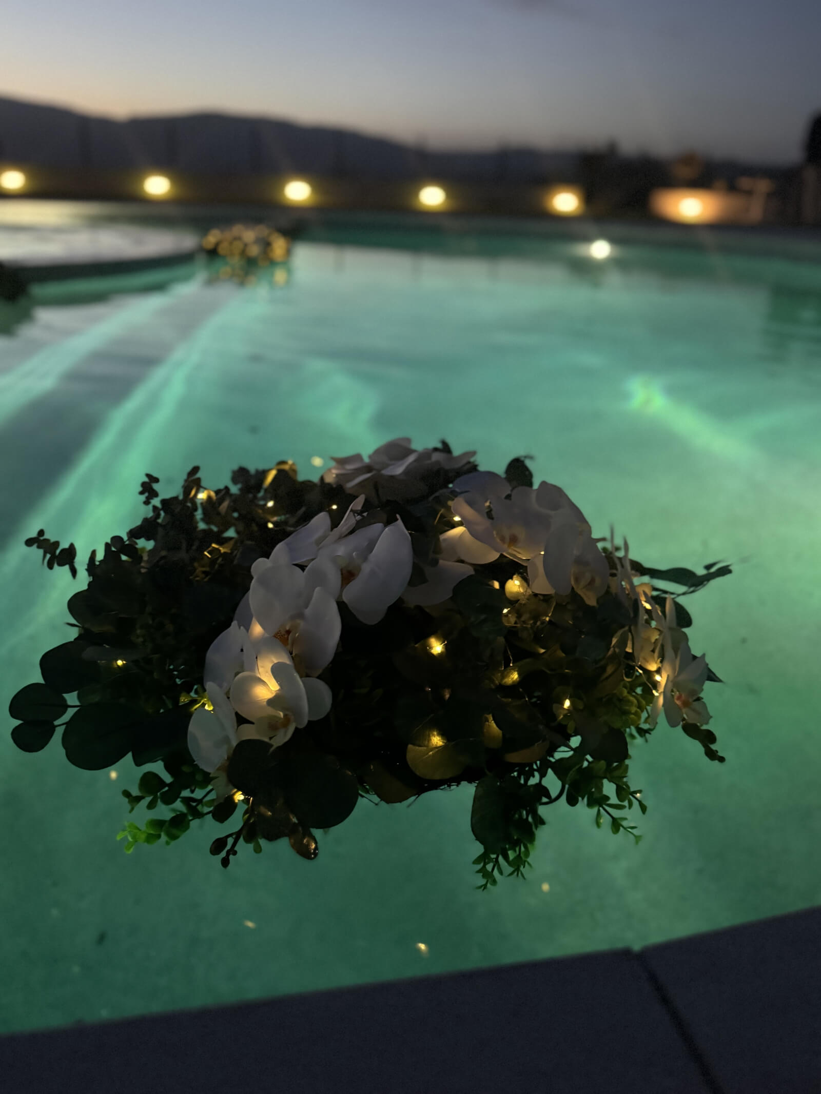 Floating bouquet glowing in pool light at an evening wedding
