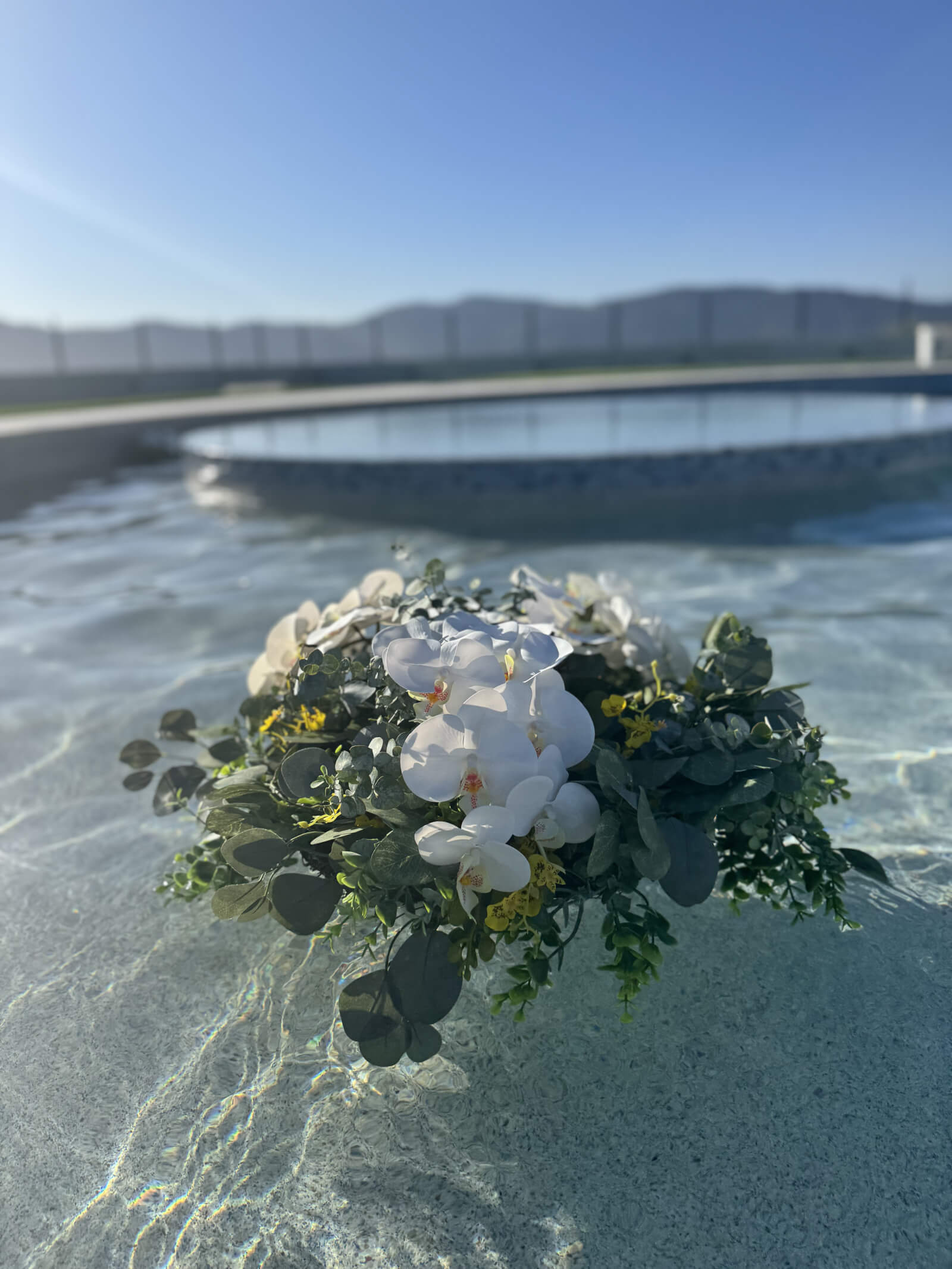 Floating bouquets clustered at the edge of a pool at a wedding